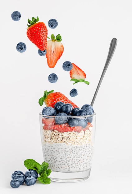 Bacche fresche che cadono nel bicchiere con budino di chia e avena. Mangiare sano.