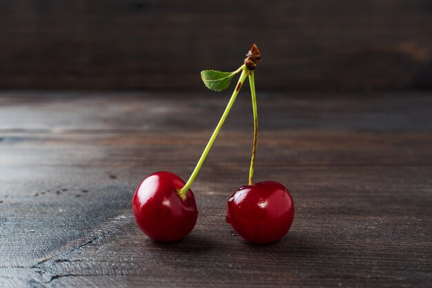 Bacche fresche mature della ciliegia su un ramo con una foglia su un fondo rustico di legno.