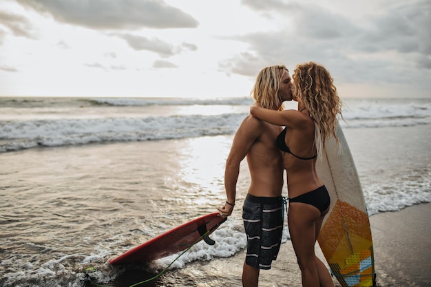 Baci di coppia durante il tramonto Uomo e donna in possesso di tavole da surf