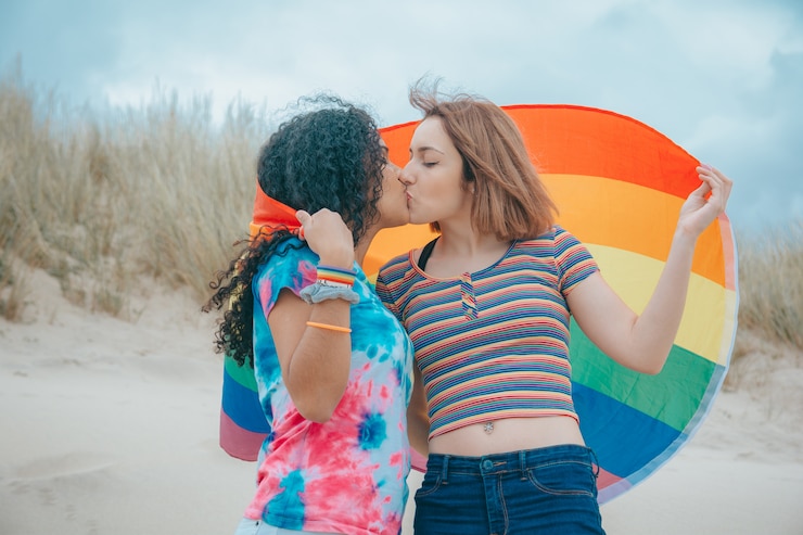 Foto baciare giovane coppia lesbica gay pride flag commovente su una spiaggia sabbiosa