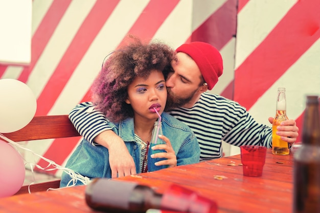 Bacio del mattino. Giovane stanco che bacia la sua ragazza assonnata mentre era seduto al tavolo dopo la festa notturna con lei