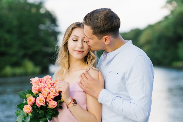 Bacio dolce e tremendo sulla guancia di un giovane ragazzo e di una bella ragazza bionda sul lago. Primo appuntamento e amore