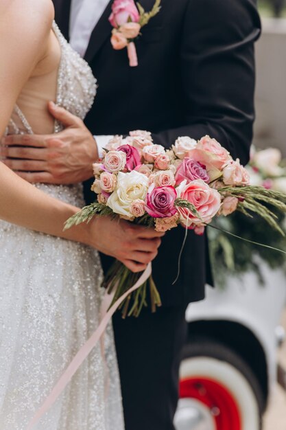 Bacio sensuale dei due nel giorno del loro matrimonio vicino a un'auto retrò con fiori