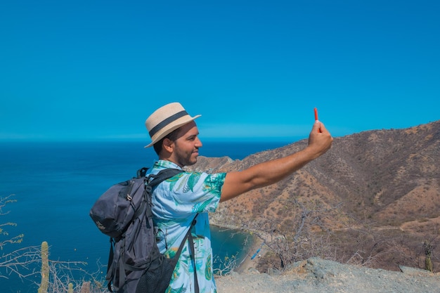 Backpacker usando il suo smartphone in vacanza. uomo che tiene un telefono cellulare con un mare sullo sfondo. Concetto di viaggio