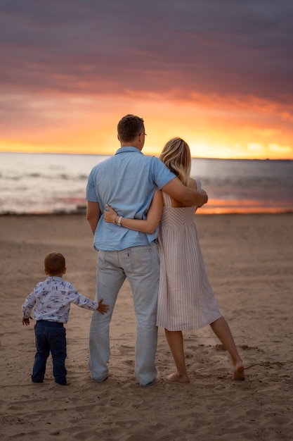 backview di coppia felice che abbraccia sulla spiaggia al tramonto bambino in piedi da loro