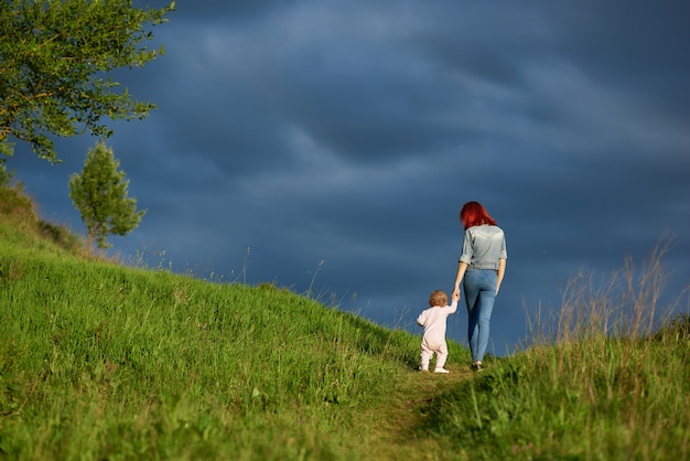 Backview di giovane madre che va con la piccola figlia nel campo di estate.