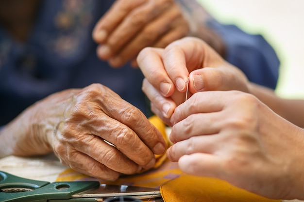 Badante che tiene il filo dell'ago per la donna anziana nella terapia occupazionale dei mestieri del panno