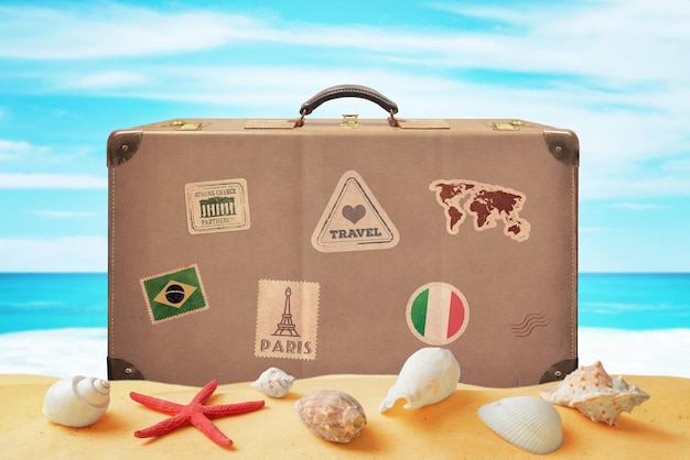 Bagagli del viaggiatore con adesivi sulla spiaggia circondata da conchiglie Mare sullo sfondo Concetto di vacanza tropicale