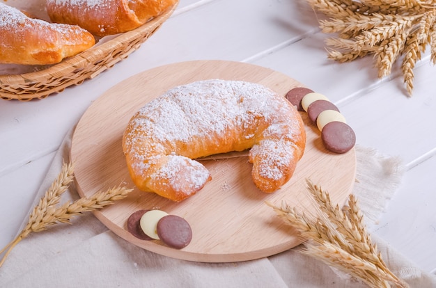 Bagel fresco e gustoso con ripieno di cioccolato su tavola di legno rotonda su fondo di legno bianco