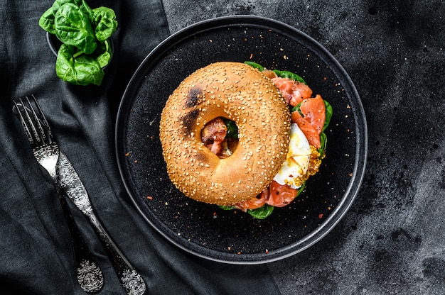 Bagel salmone affumicato toast con formaggio a pasta molle, spinaci e uovo. Superficie nera. Vista dall'alto