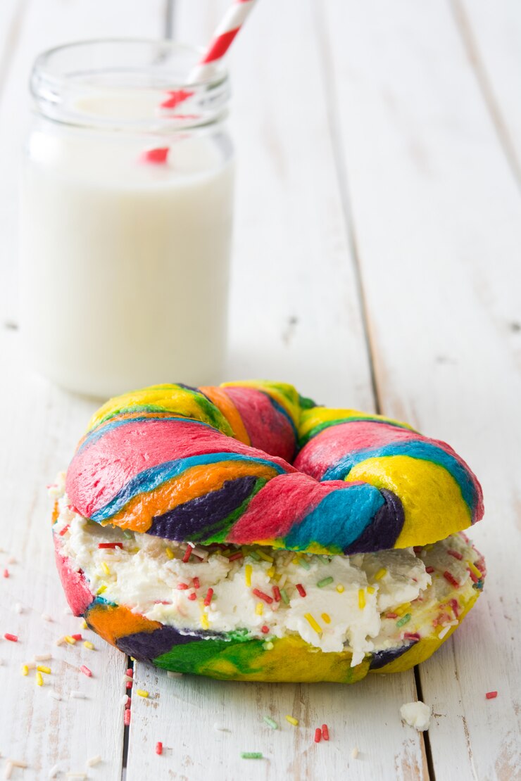 Photo bagel warna-warni dengan keju dan taburan serta susu di atas meja kayu putih