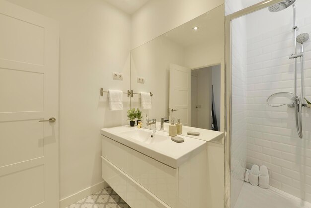 Bagno con lavabo monopezzo in porcellana bianca, grande mobile in legno a specchio senza cornice con cassetti e box doccia con porta in vetro
