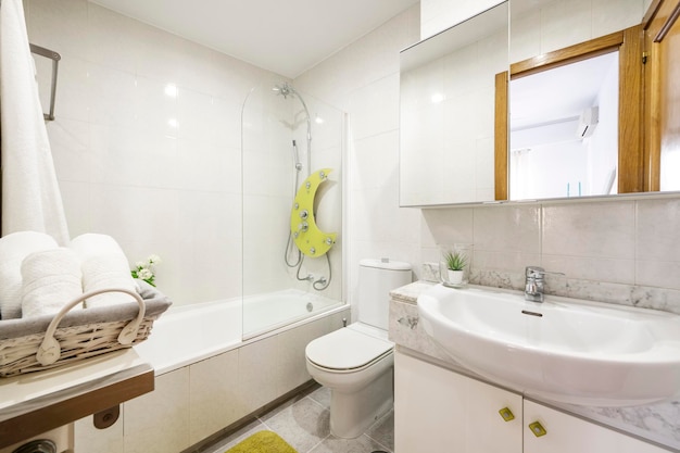 Bagno con mobili bianchi, servizi igienici in porcellana bianca, doccia con divisorio in vetro e asciugamani arrotolati
