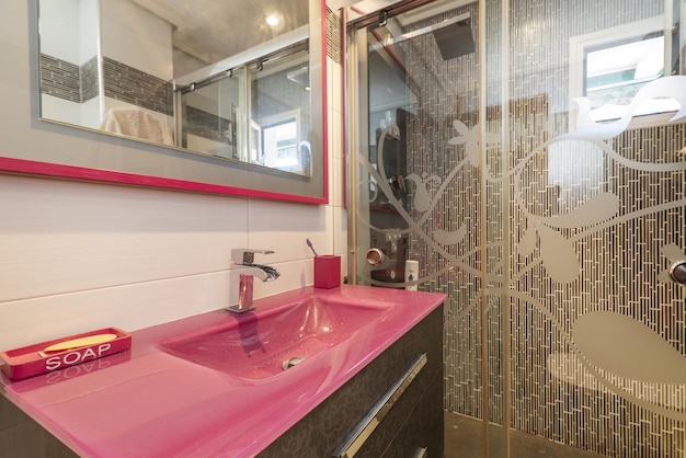 Bagno con pareti e pavimenti piastrellati bianchi e un mobile da bagno in legno scuro con lavabo in vetro temperato rosso con specchio abbinato e cornice in legno