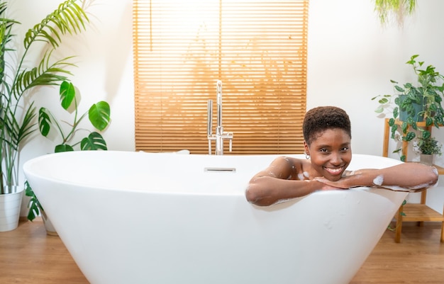 Bagno di lusso ritratto di una donna africana attraente che si rilassa nella vasca da bagno nell'accogliente bagno di casa