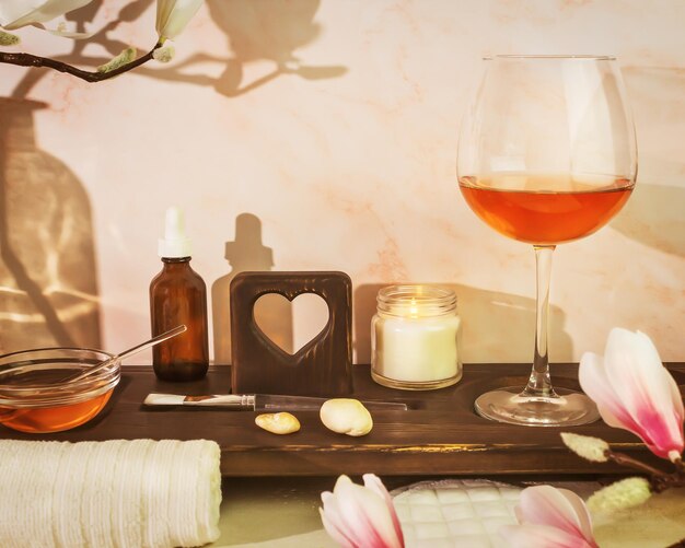 Bagno sostenibile con accessori spa, candela di siero e bicchiere di vino rosa su una tavola di legno