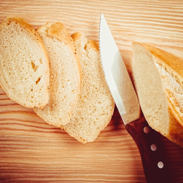 Baguette appena sfornata affettata su tagliere di legno coltello vista dall'alto piatto laico