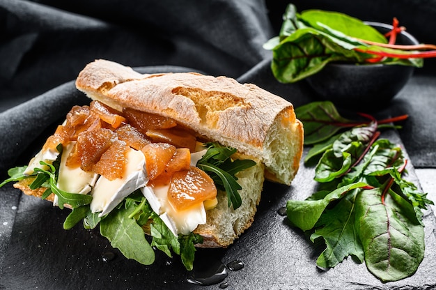 Baguette con formaggio di capra, marmellata di pere, bietole e spinaci. Sfondo nero. Vista dall'alto.