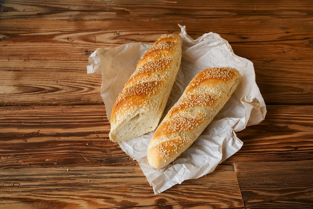 Baguette di pane cosparsa di sesamo e sesamo con carta da imballaggio su un tavolo di legno