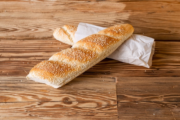 Baguette di pane cosparsa di sesamo e sesamo con carta da imballaggio su un tavolo di legno