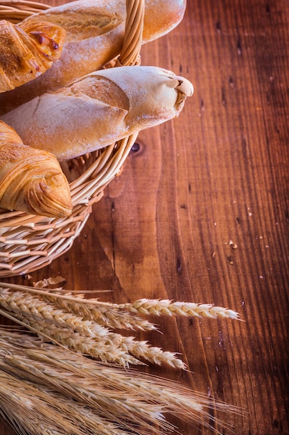 Baguette e croissant in cesto di vimini spighe di segale di grano su tavola di legno vintage cibo e bevande concetto