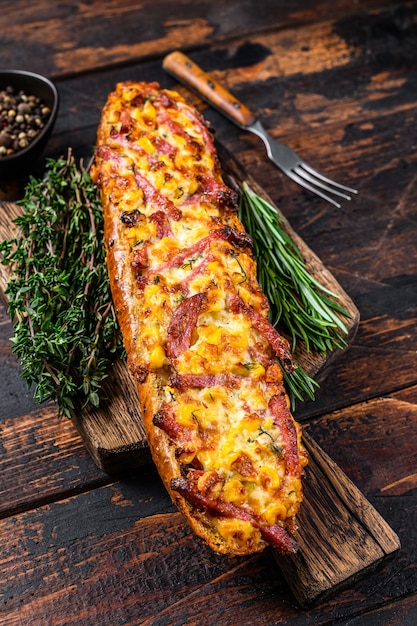 Baguette farcita con prosciutto, pancetta, verdure e formaggio su tavola di legno. Fondo in legno scuro. Vista dall'alto.