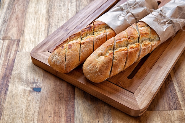 Baguette francesi avvolte in carta da imballaggio su un tagliere. Fondo in legno