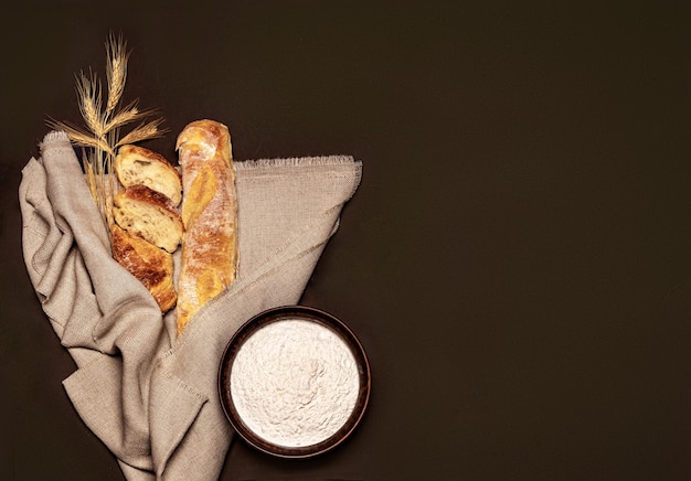 Baguette su sfondo marrone con spighe di grano e farina