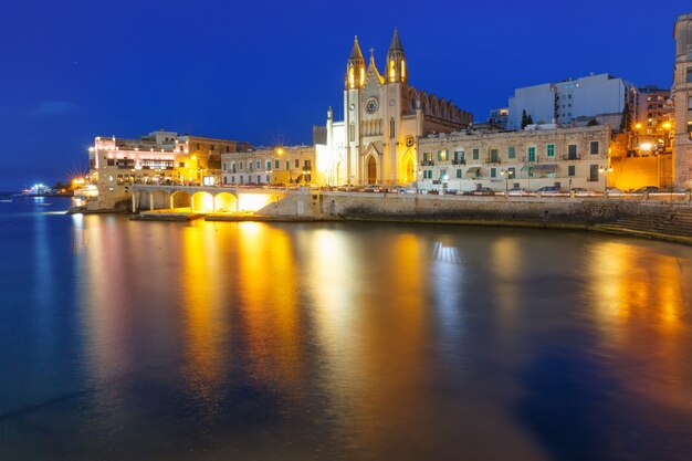 Baia di Balluta e chiesa neogotica di Nostra Signora del Monte Carmelo, chiesa parrocchiale di Balluta, durante l'ora blu serale, Saint Julien, Malta