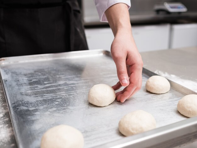 Baker lavora con l'impasto su un piano di lavoro in metallo. Cuoco professionista che prepara panini o panini