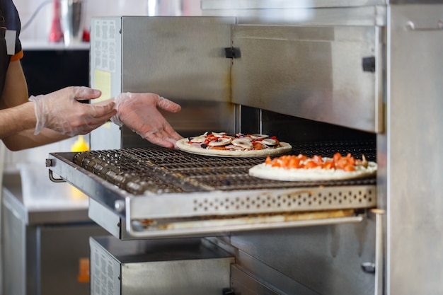 Baker mette la pizza cruda in un forno industriale