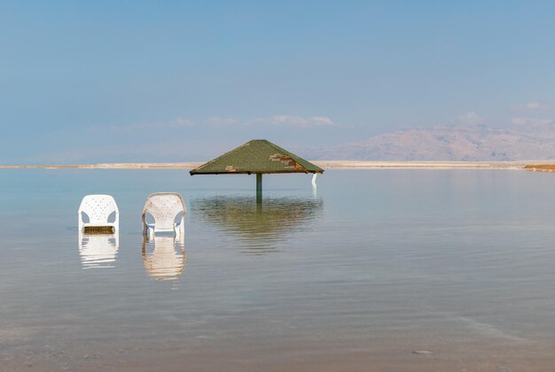 Baldacchino dal sole e due sedie nell'acqua del Mar Morto