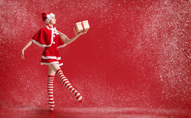 Ballerina ballerina in scarpe da punta con un regalo in mano vestita da Babbo Natale su uno sfondo rosso.