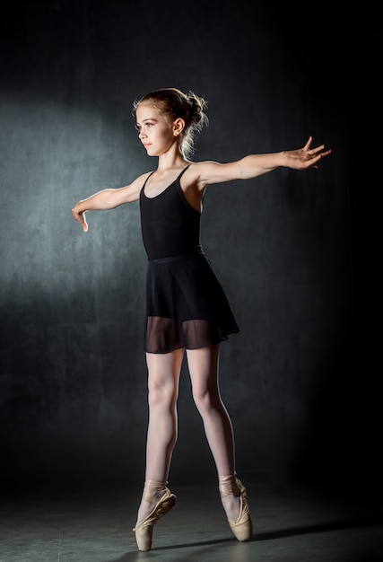 Ballerina. Bambina sveglia che posa e che balla nello studio. Una piccola ballerina. Sfondo scuro Vestito nero.