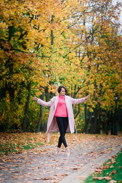 Ballerina che balla in natura tra le foglie autunnali in cappotto biondo.