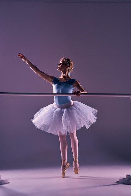 Ballerina classica in tutù bianco alla sbarra di balletto su uno sfondo lilla