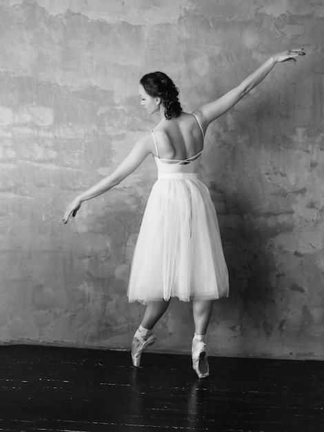 Ballerina del ballerino di balletto in bella gonna bianca del tutu del vestito che posa nello studio del sottotetto