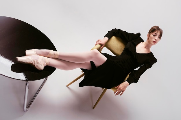 Ballerina in abito nero siede sexy a un tavolino da caffè con le gambe piegate su di esso in sterline