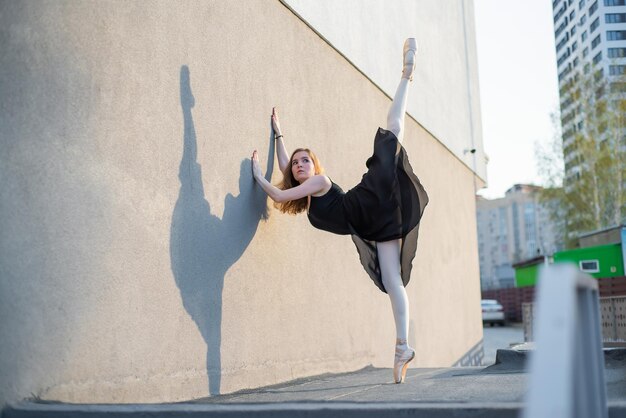 Ballerina in tutù in posa in piedi vicino al muro Bella giovane donna in abito nero e punta che balla fuori Splendida ballerina che esegue un ballo all'aperto