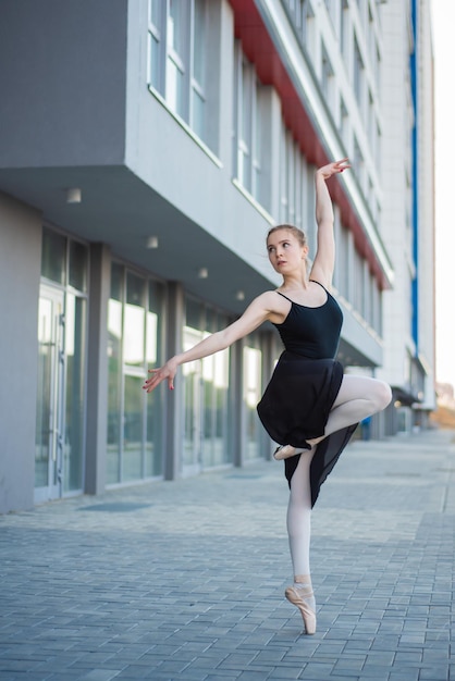 Ballerina in tutù in posa sullo sfondo di un edificio residenziale Bella giovane donna in abito nero e scarpe da punta che balla balletto fuori