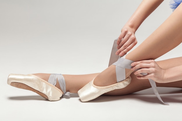 Ballerina legare scarpe da punta mentre è seduto isolato su bianco di sfondo per studio closeup
