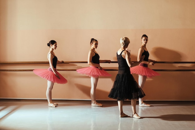 Ballerini femminili che tengono su una sbarra mentre praticano con l'istruttore di balletto alla scuola di ballo