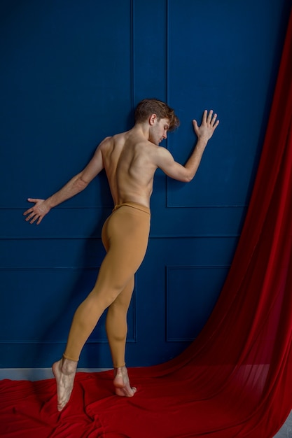 Ballerino di balletto maschio, esibendosi in studio di danza, pareti blu e panno rosso sullo sfondo