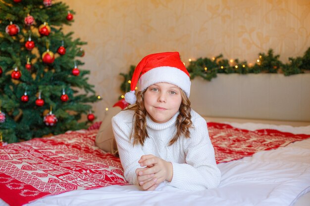 Bambina a casa sdraiata sul letto in camera da letto indossando il cappello di Babbo Natale