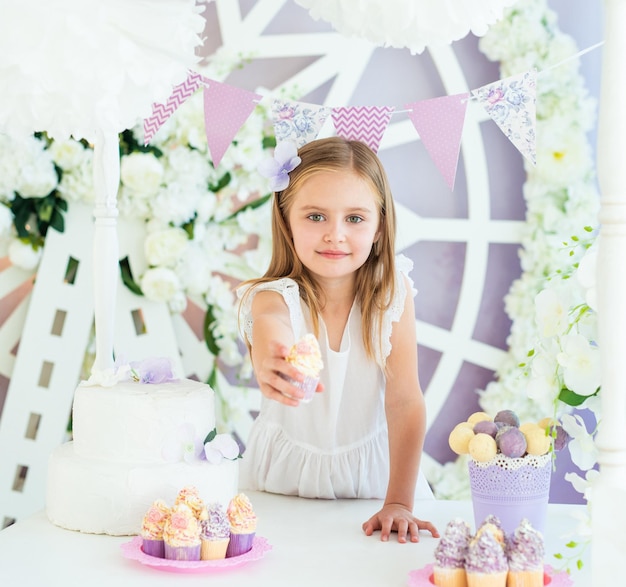 Bambina abbastanza sorridente che tiene una torta gustosa nel bellissimo candy bar decorato