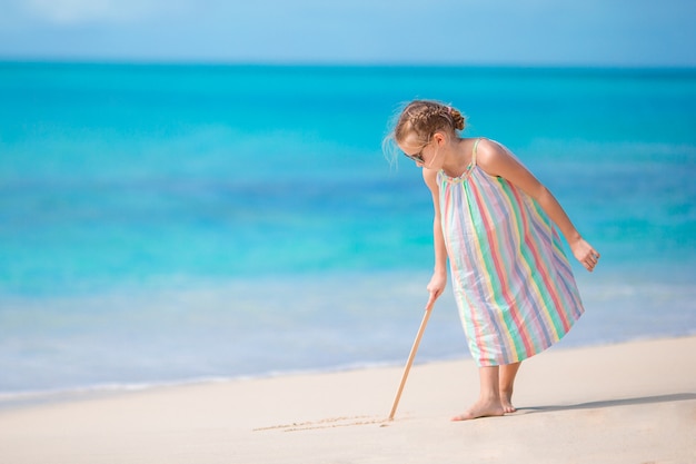 Bambina adorabile alla spiaggia durante le vacanze estive che attingono sabbia