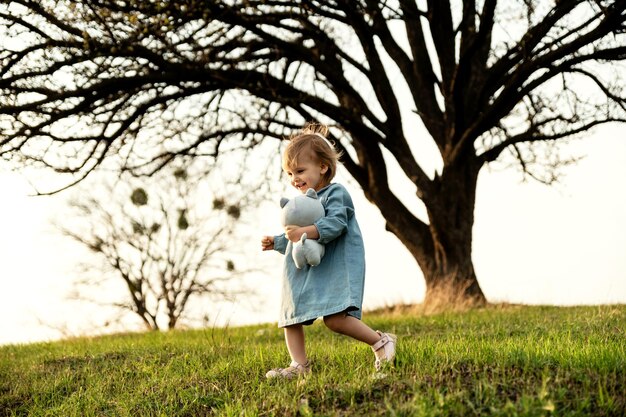 Bambina adorabile che gioca con un peluche all'aperto nel parco al tramonto infanzia felice