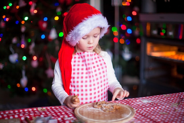 Bambina adorabile che mangia la pasta per i biscotti dello zenzero in cucina