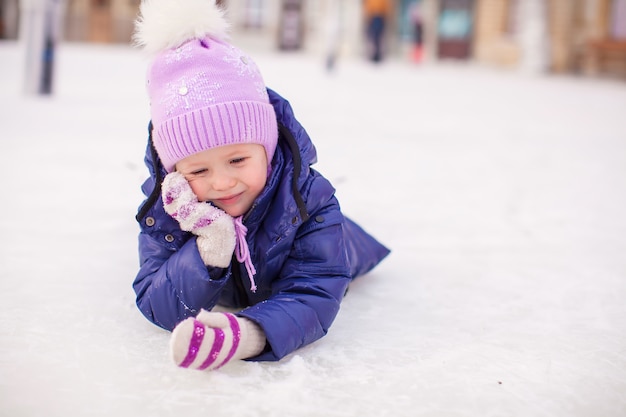 Bambina adorabile che pone sulla pista di pattinaggio dopo la caduta