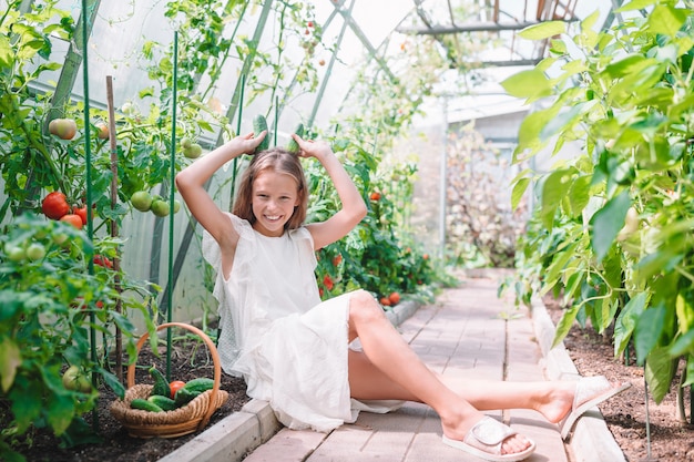 Bambina adorabile che raccoglie i cetrioli e i pomodori in serra.